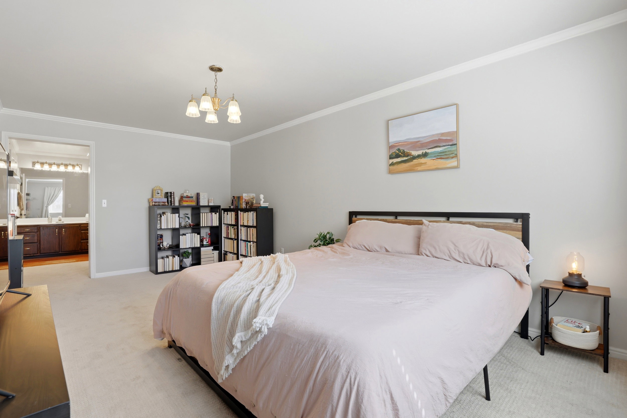 Carpeted bedroom featuring crown molding, hanging lights, and ensuite bathroom