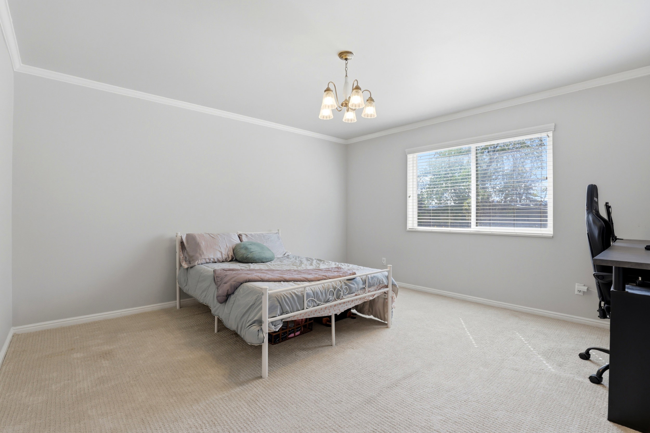 Bedroom featuring light colored carpet, ornamental molding, hanging lights, and a desk