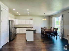Kitchen featuring white cabinets, stainless steel appliances, a center island with sink, dark wood finished floors, and dark countertops
