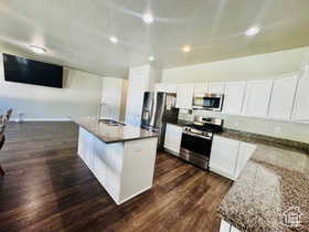 Kitchen featuring stainless steel appliances, dark wood-type flooring, white cabinetry, and dark stone counters