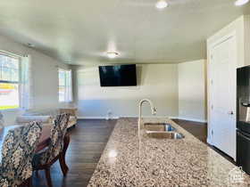 Kitchen with light stone countertops, dark wood-style flooring, black fridge with ice dispenser, a kitchen island with sink, and a textured ceiling