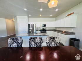 Kitchen with stainless steel appliances, a center island with sink, white cabinetry, recessed lighting, and dark wood-style floors