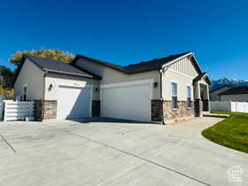 View of front of home with stone siding, a garage, concrete driveway, and stucco siding