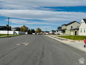 View of asphalt street with sidewalks, a residential view, curbs, and street lighting