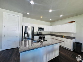 Kitchen featuring stainless steel appliances, a kitchen island with sink, white cabinets, dark stone counters, and dark wood finished floors