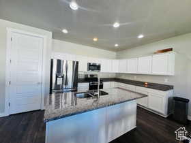 Kitchen featuring stainless steel appliances, a kitchen island with sink, white cabinets, dark stone counters, and dark wood finished floors