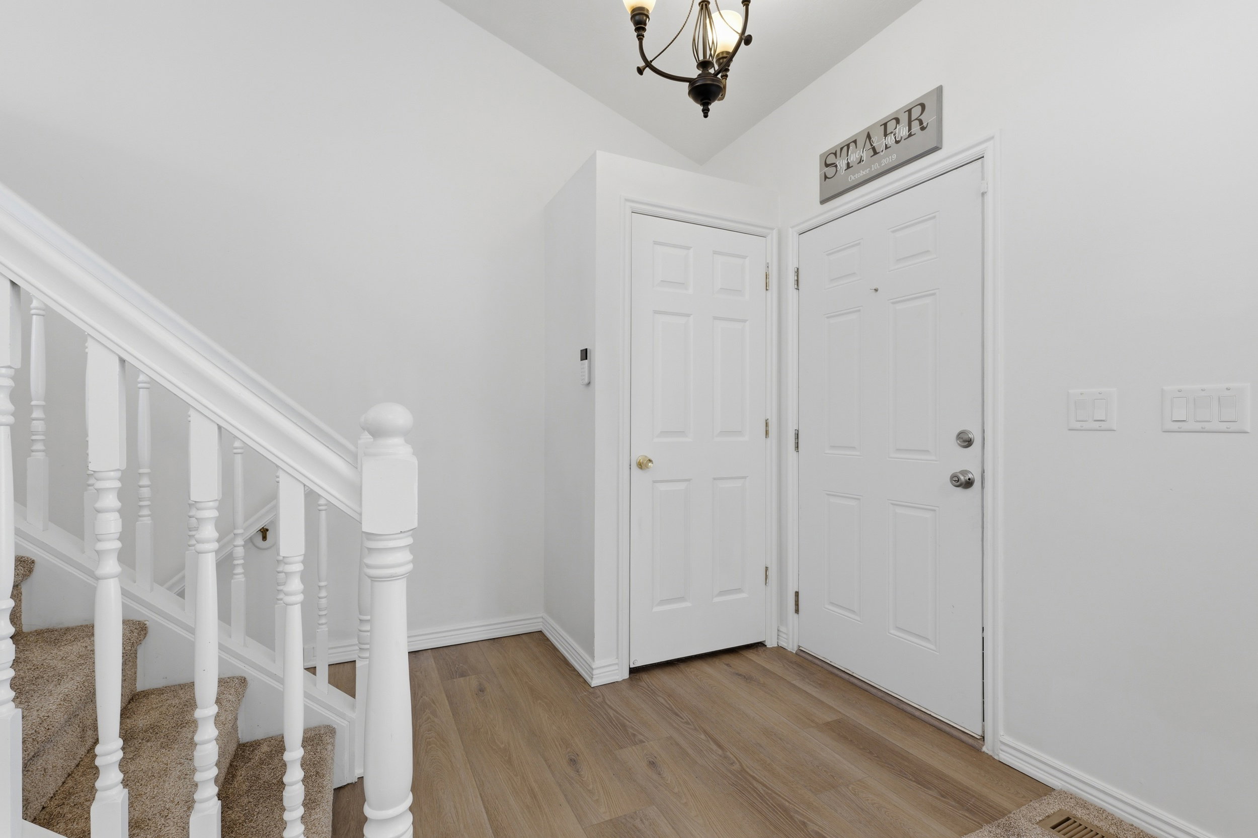 Entryway featuring wood-finish flooring, white paneled doors, and a staircase with white balusters and carpeted treads
