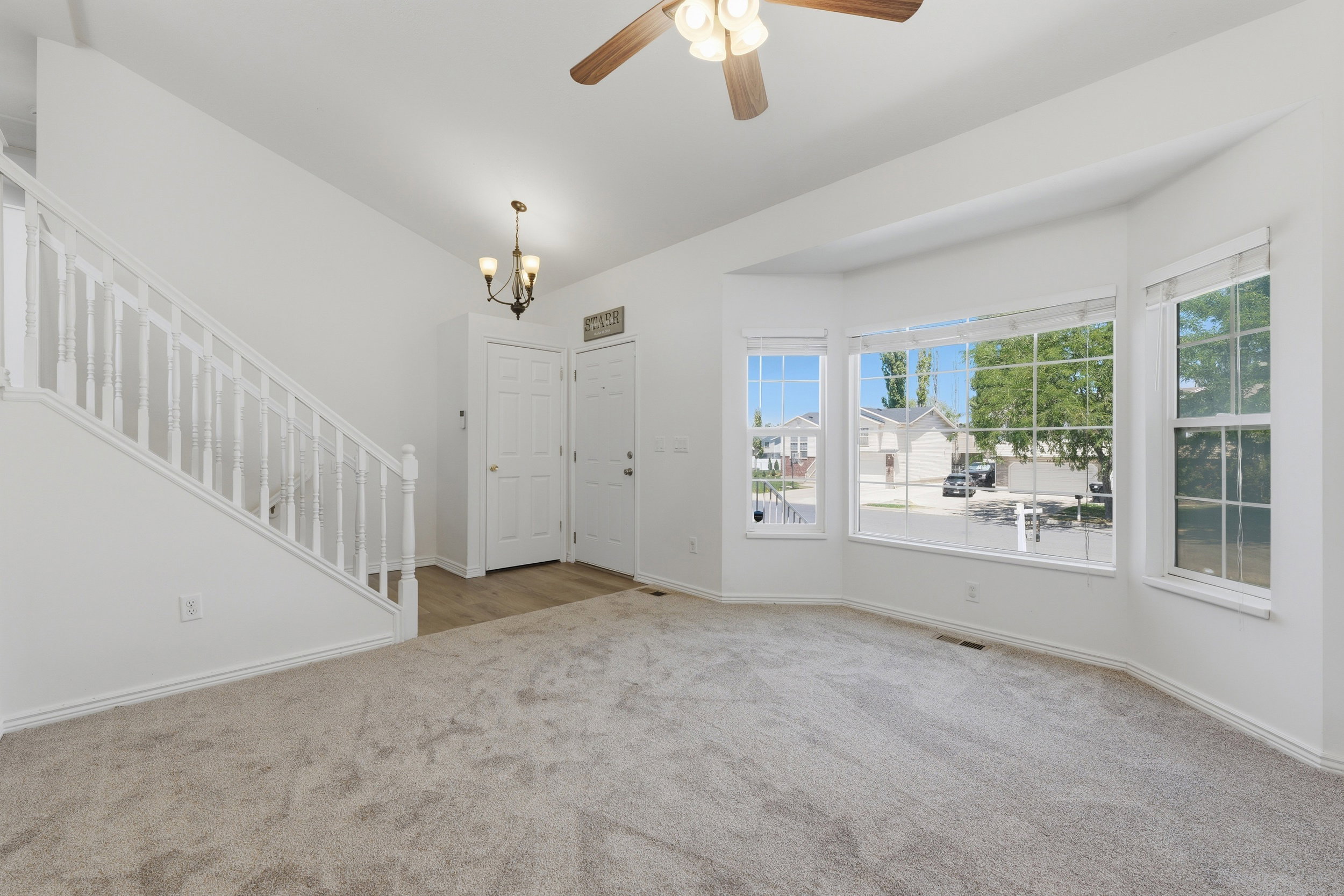 Bright living area featuring a large bay window, neutral carpeting, and a ceiling fan