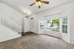 Foyer featuring dark carpet, ceiling fan, a chandelier, and lofted ceiling
