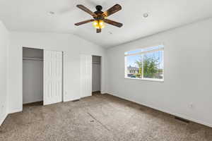 Unfurnished bedroom featuring multiple closets, a ceiling fan, carpet, and lofted ceiling