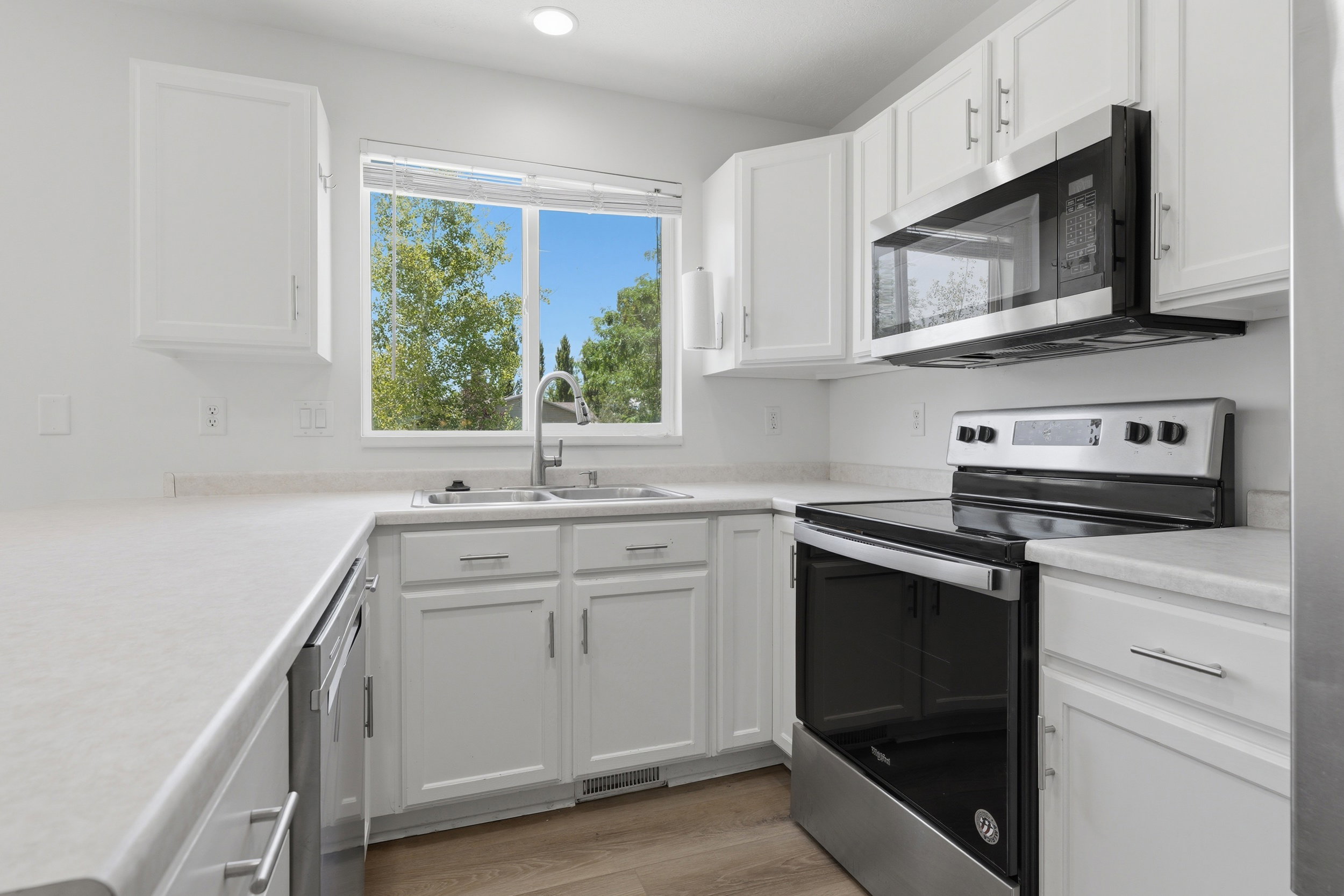 Kitchen featuring white cabinetry, light-toned countertops, a stainless steel range with an overhead microwave, and wood-finish flooring