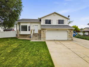Split level home featuring concrete driveway, an attached garage, and stone siding