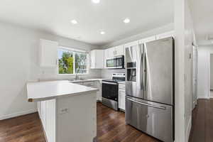 Kitchen with a peninsula, stainless steel appliances, light countertops, dark wood-style floors, and recessed lighting