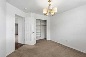 Unfurnished bedroom with suspended lighting, dark carpet, and a closet