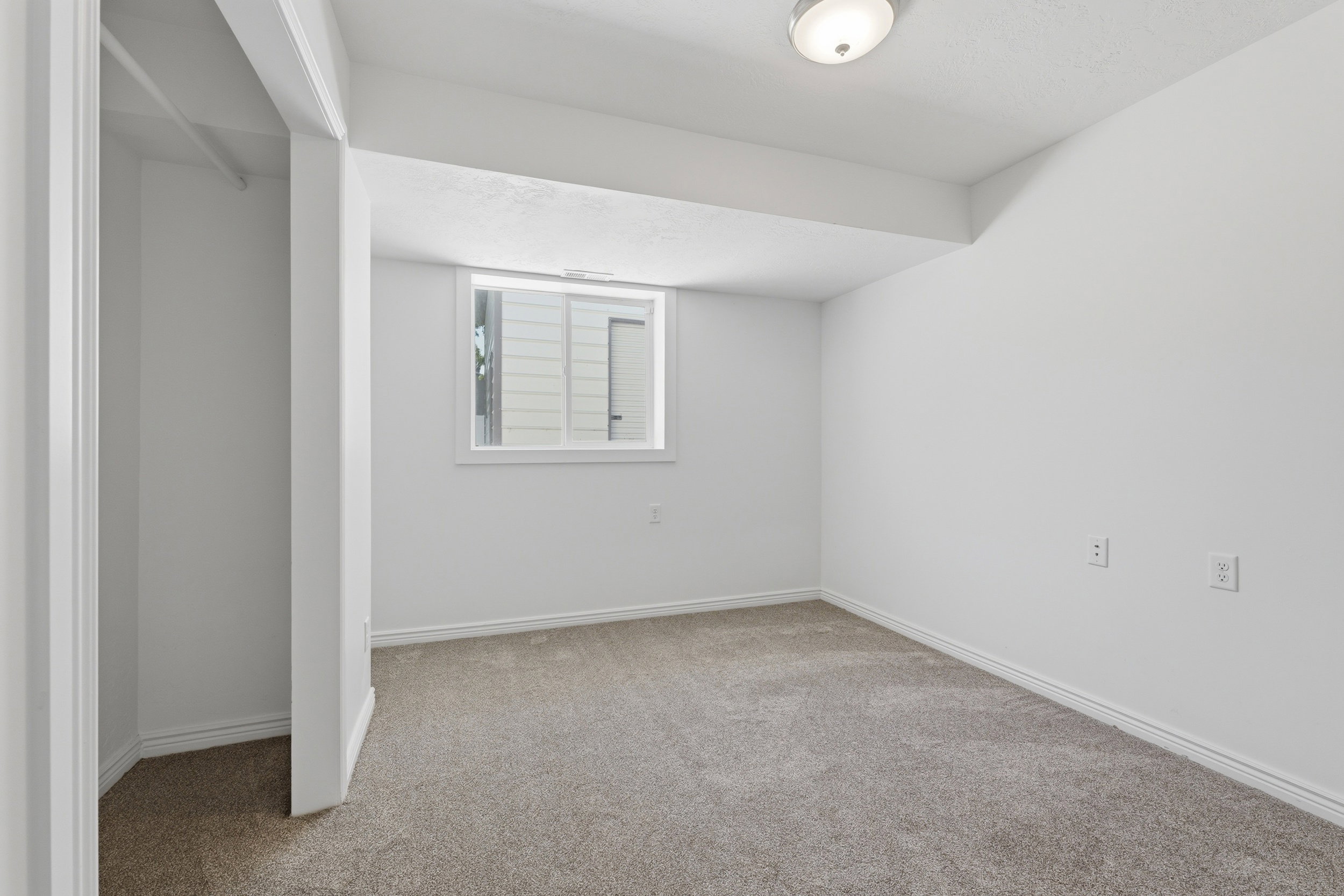 Carpeted room featuring a white-trimmed window, white walls, and a built-in closet with a hanging rod