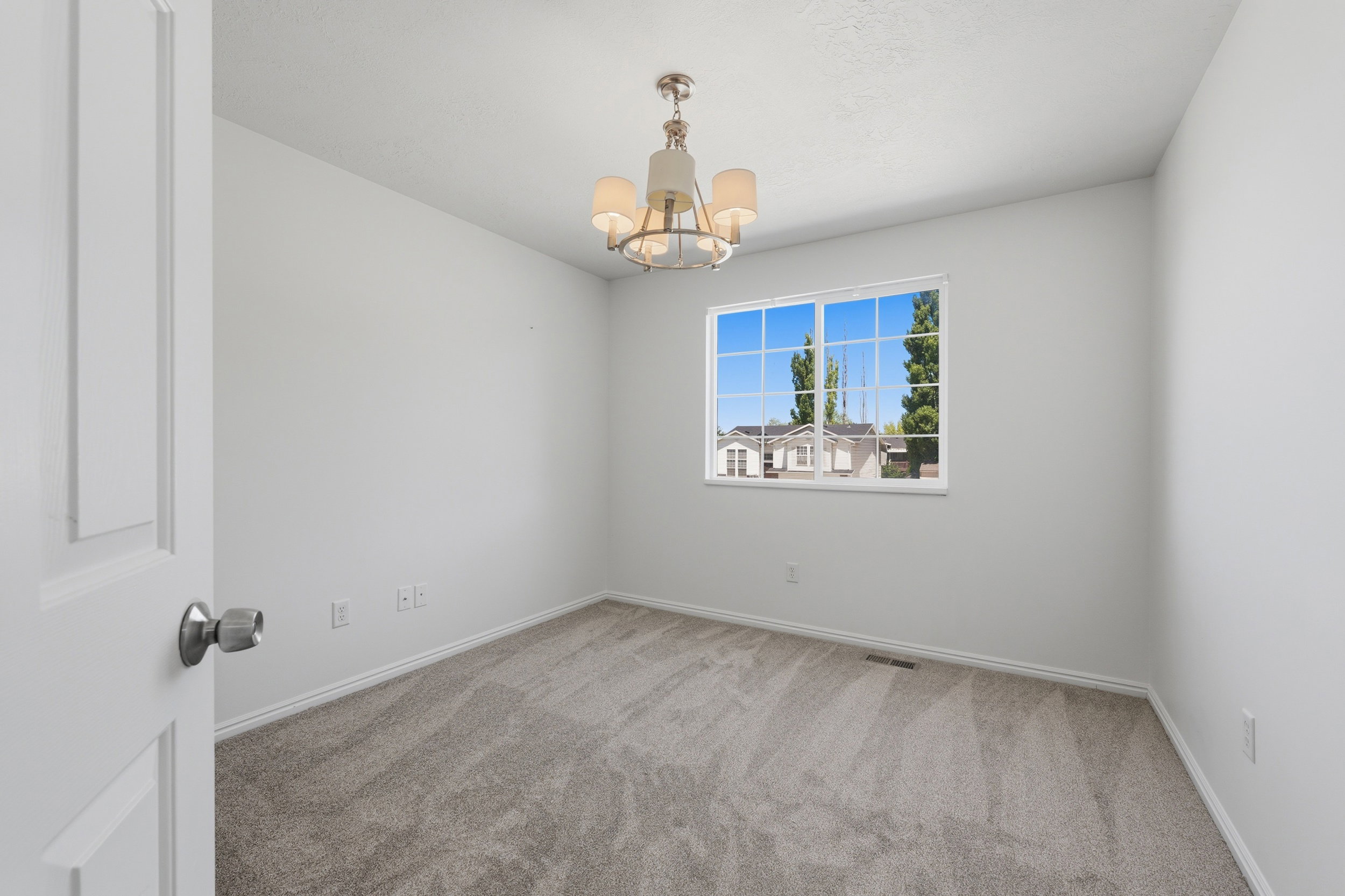 Carpeted room featuring a ceiling-mounted chandelier, a window with gridded panes, white baseboards, and light-colored walls