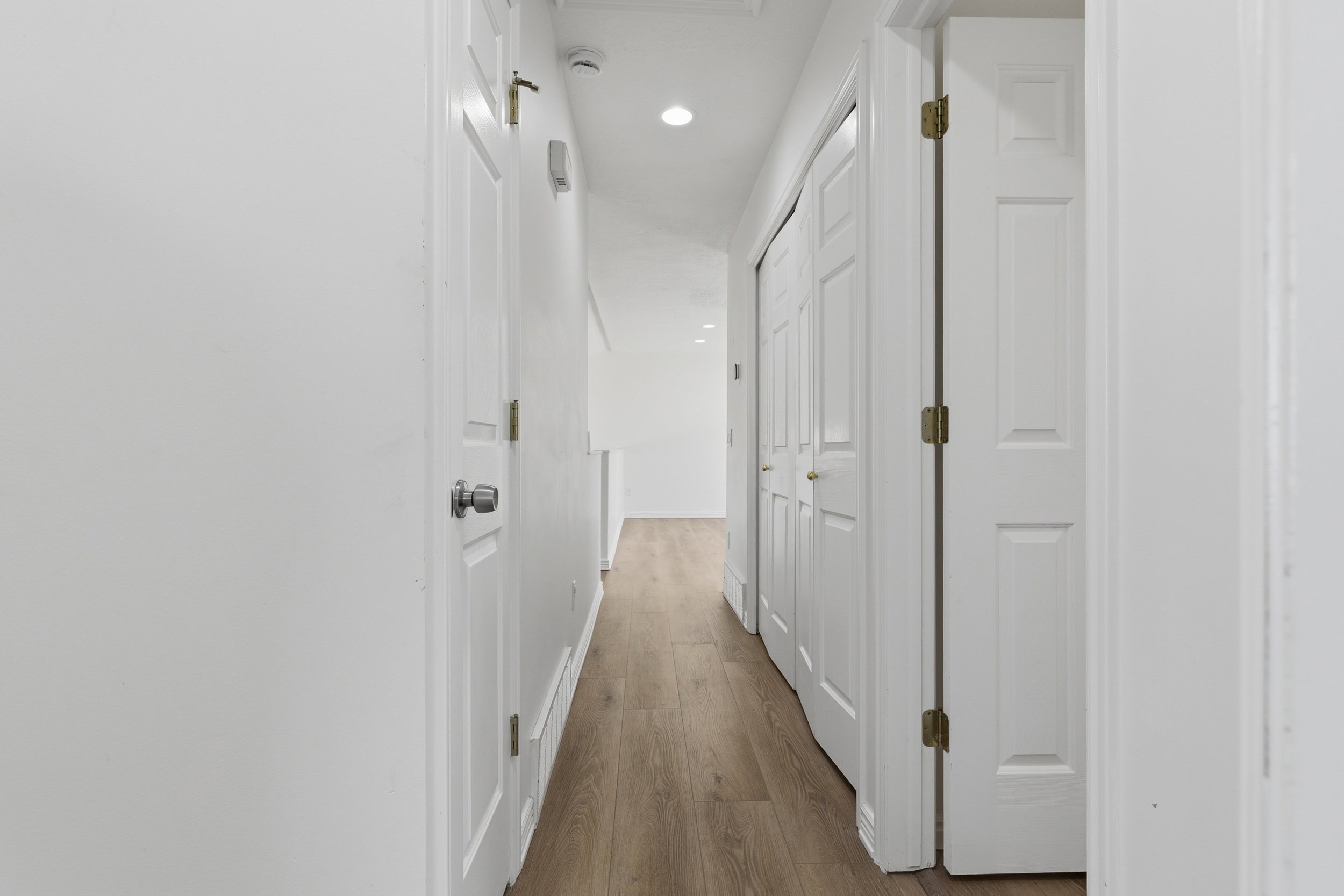 Hallway featuring wood-finish flooring, recessed lighting, white paneled doors, and bi-fold closet doors