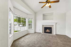 Unfurnished living room with carpet, a tiled fireplace, lofted ceiling, and ceiling fan
