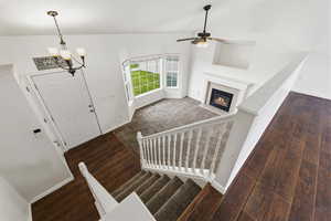 Entryway featuring dark wood-type flooring, a fireplace with flush hearth, ceiling fan, dark carpet, and vaulted ceiling