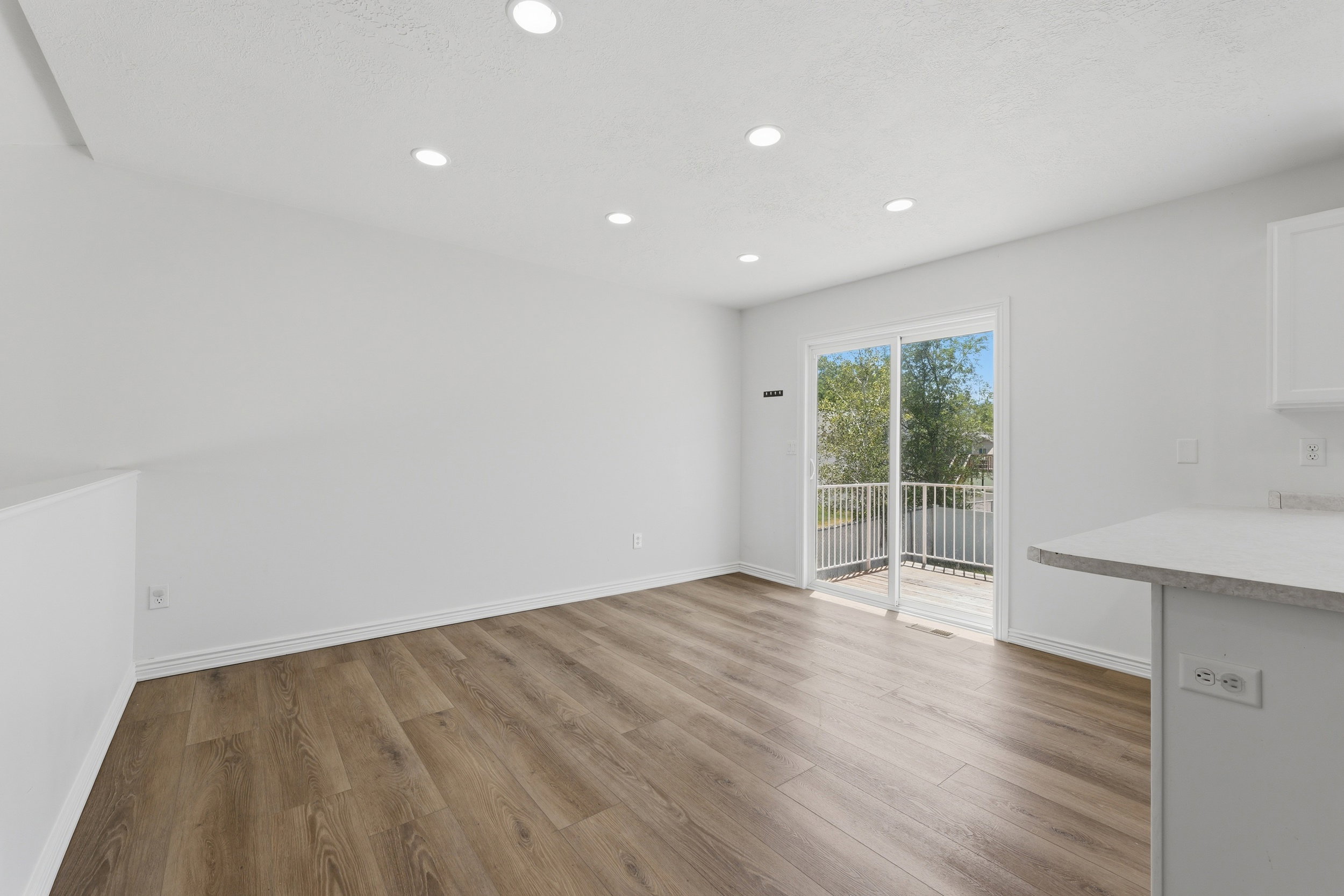 Open concept living area with wood-finish flooring, recessed lighting, and a sliding glass door leading to an outdoor deck