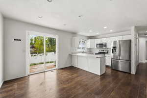 Kitchen featuring stainless steel appliances, light countertops, a peninsula, white cabinets, and dark wood-type flooring