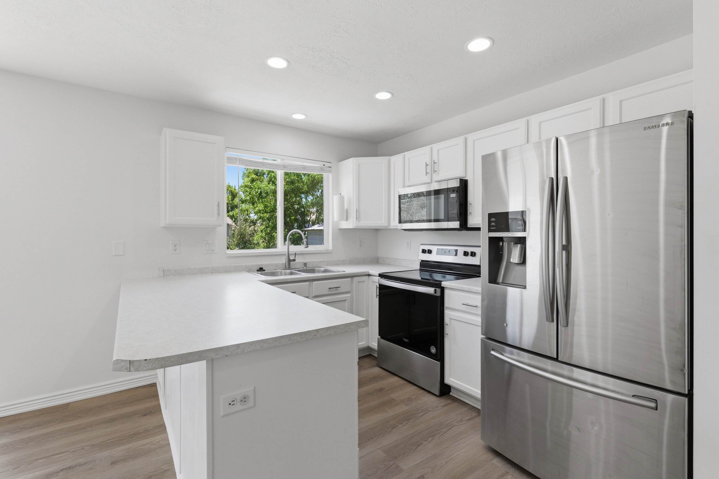 Bright kitchen featuring white cabinetry, light countertops, wood-finish flooring, a stainless steel refrigerator, and a stainless steel oven/range