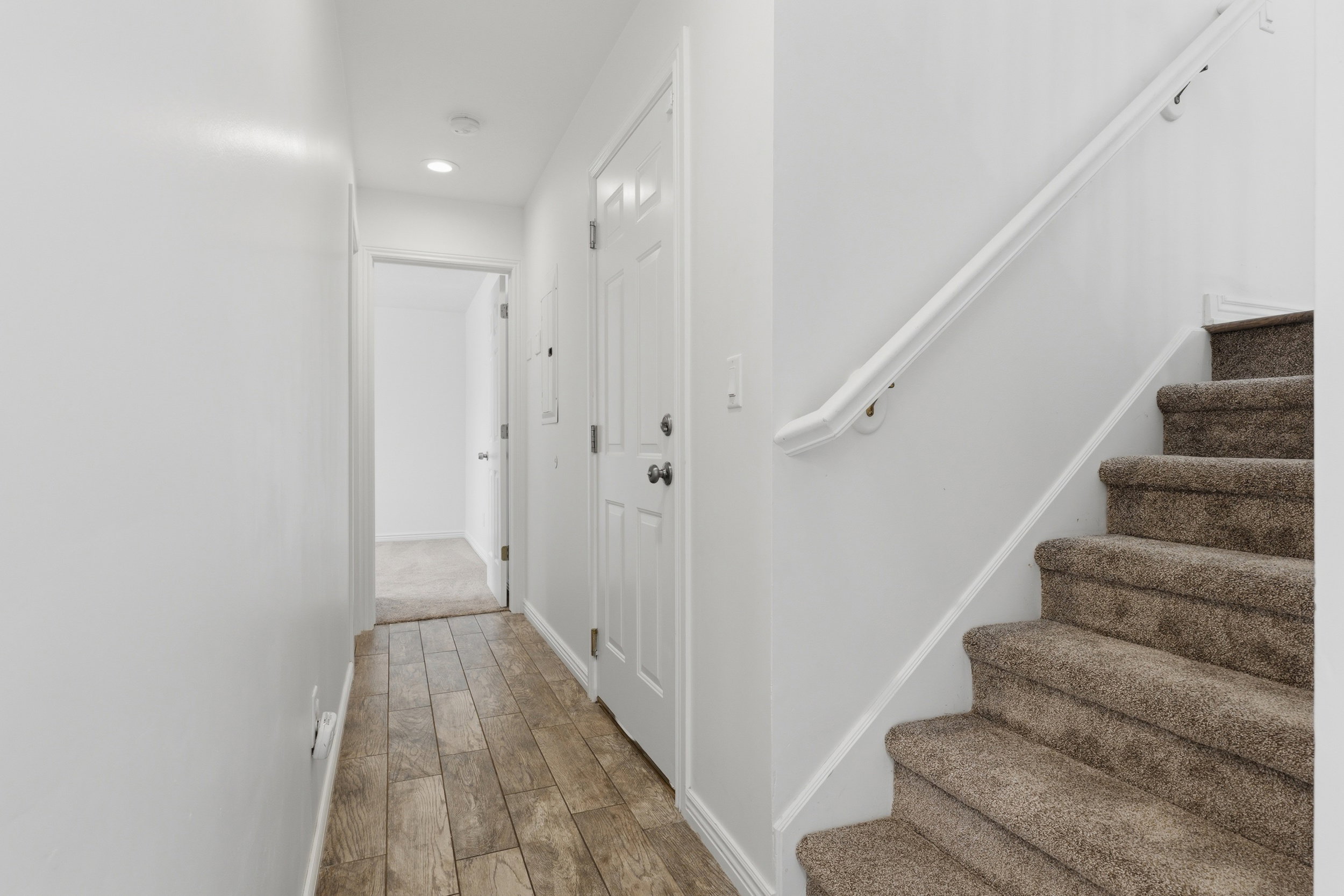 Entryway featuring wood-finish flooring, recessed lighting, white panel doors, and a carpeted staircase with white handrail