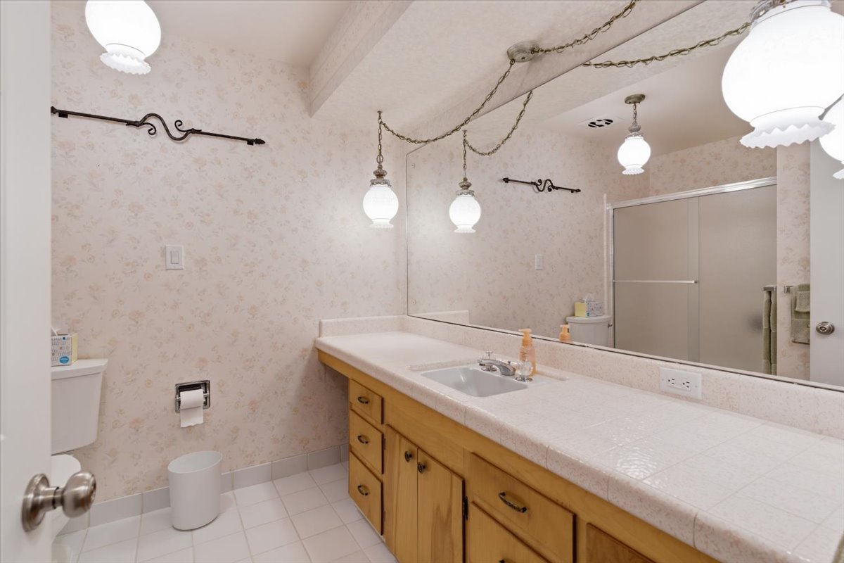 Full bath with light tile patterned floors, vanity, wallpapered walls, and a shower stall