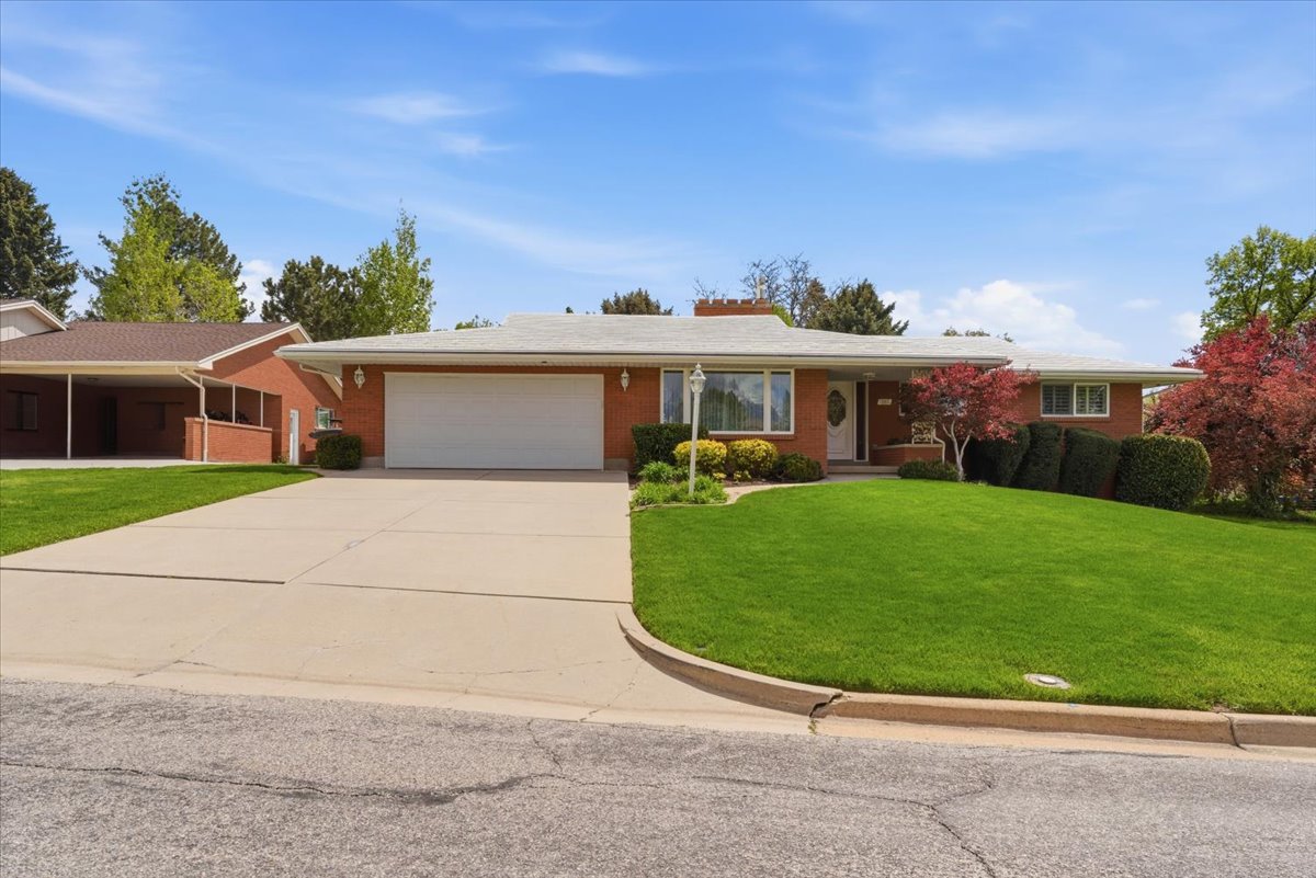Ranch-style home with a front lawn, an attached garage, driveway, and brick siding