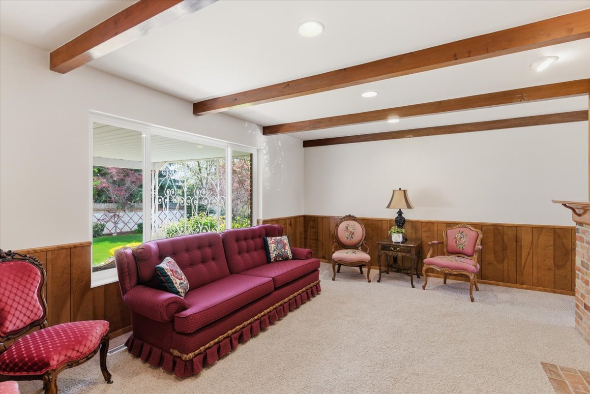 Carpeted living room featuring wooden walls, wainscoting, beamed ceiling, and recessed lighting