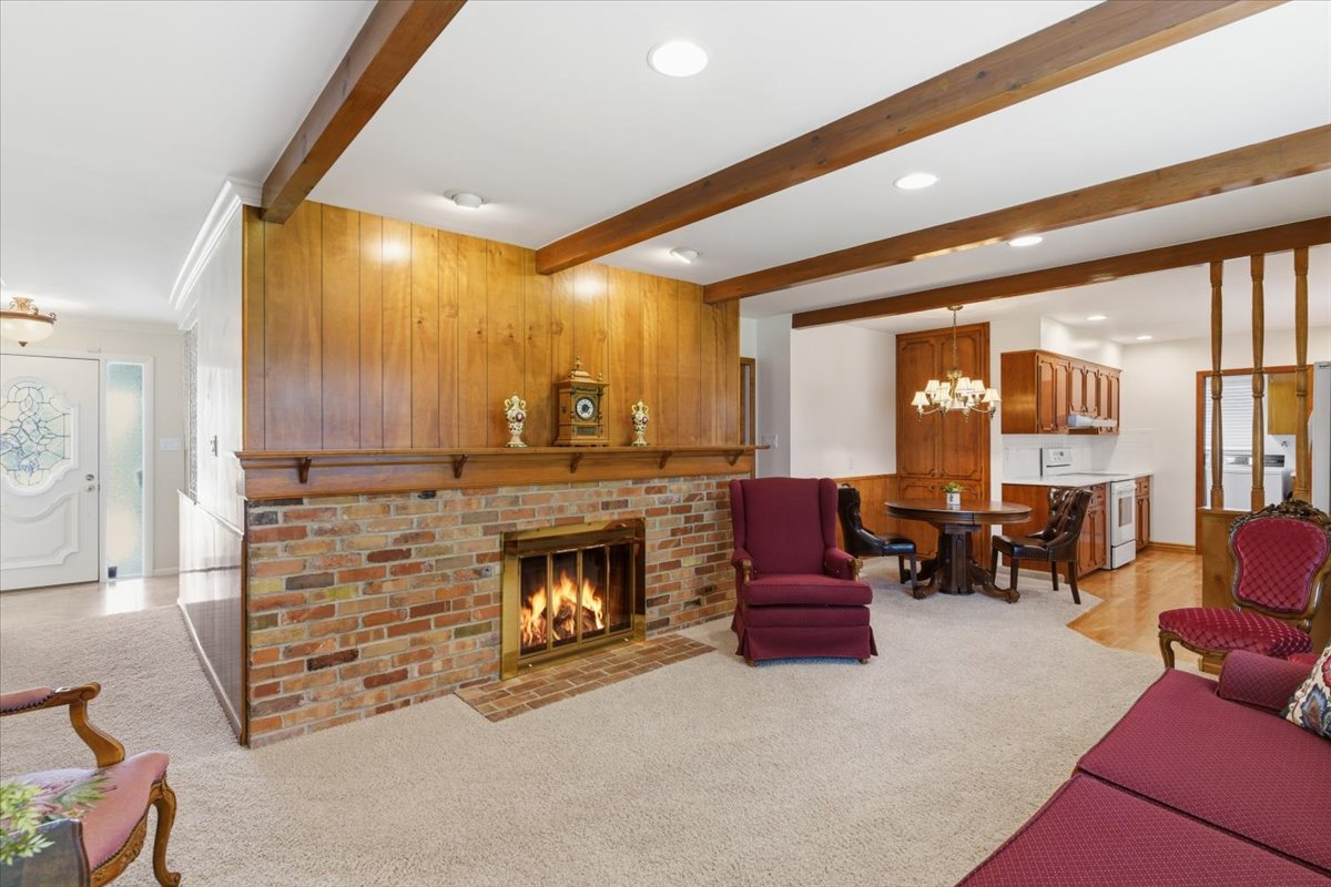 Living room featuring light carpet, a fireplace, a chandelier, and beamed ceiling