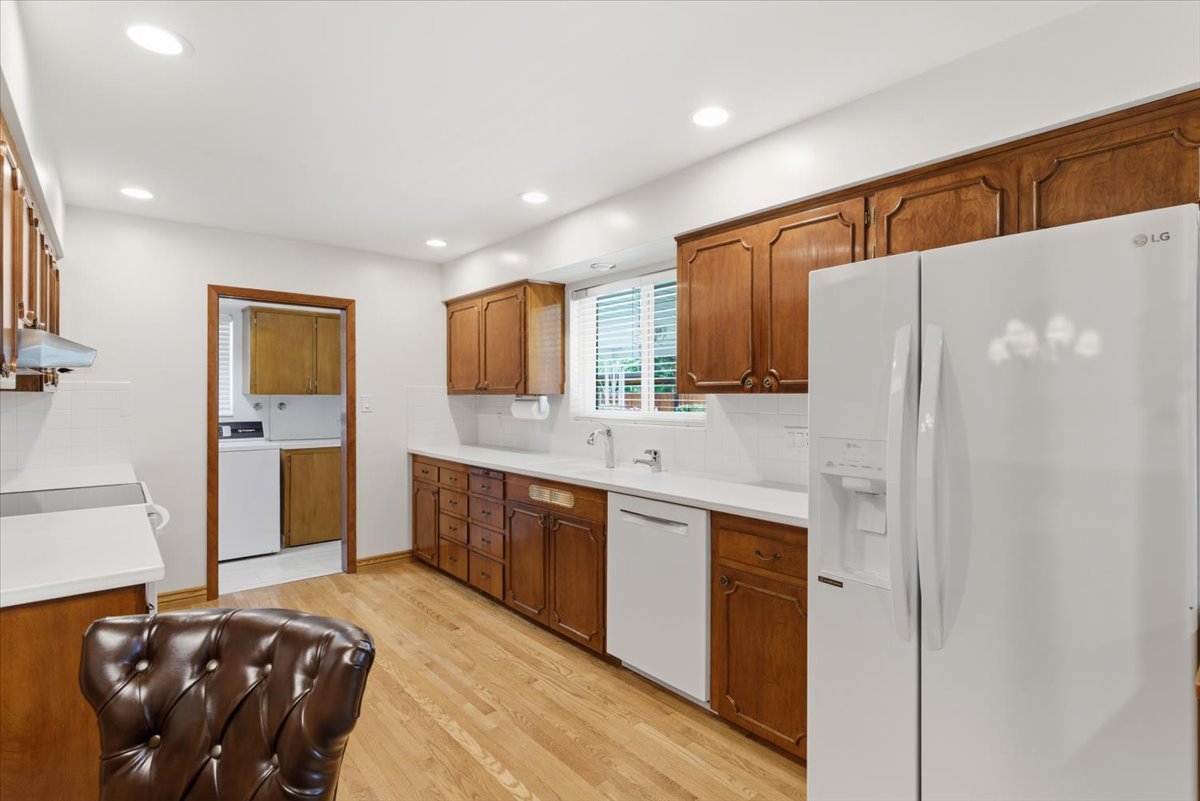 Kitchen featuring white appliances, light countertops, wood finish cabinets, light wood-type flooring, and backsplash