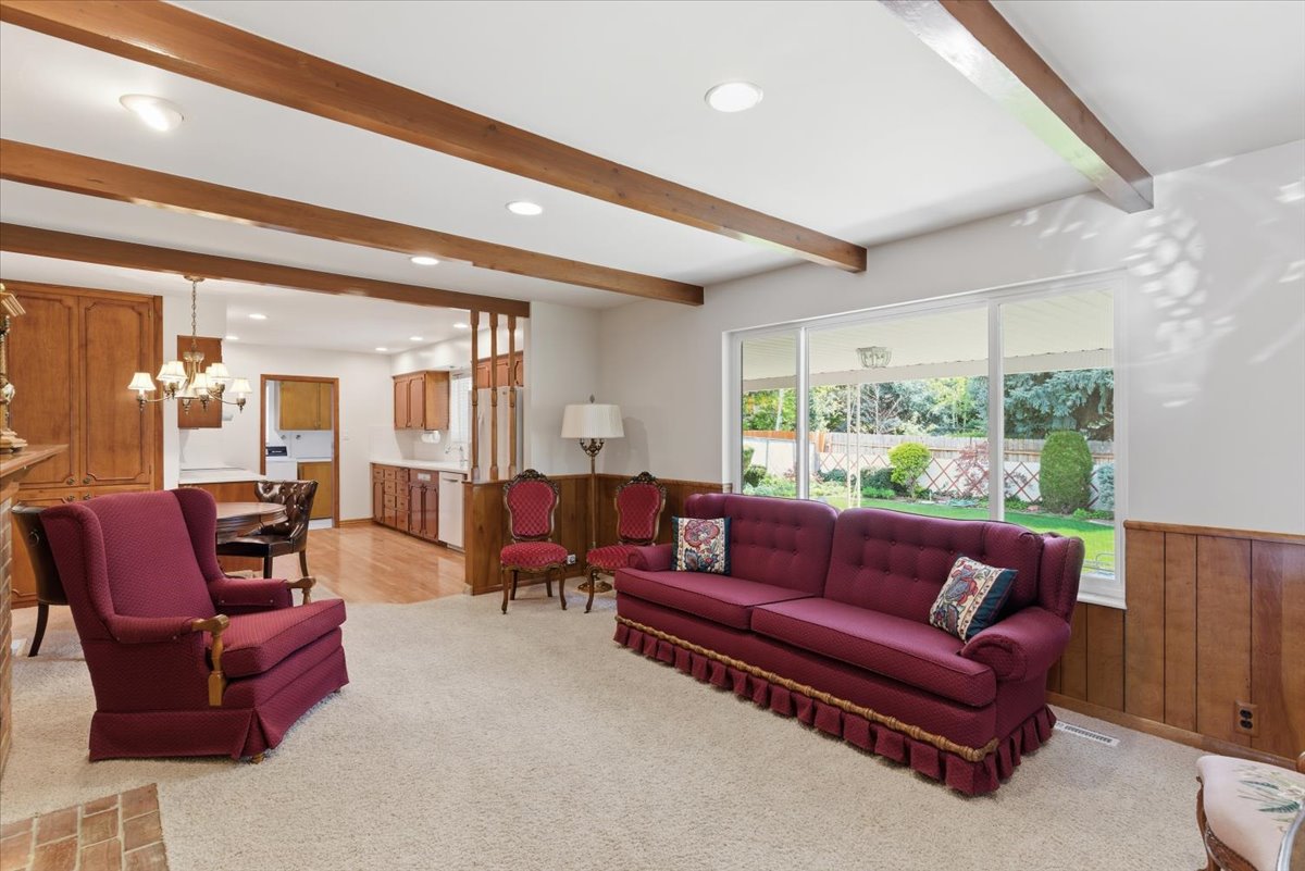 Living room featuring beamed ceiling, light colored carpet, a chandelier, wood walls, and a wainscoted wall