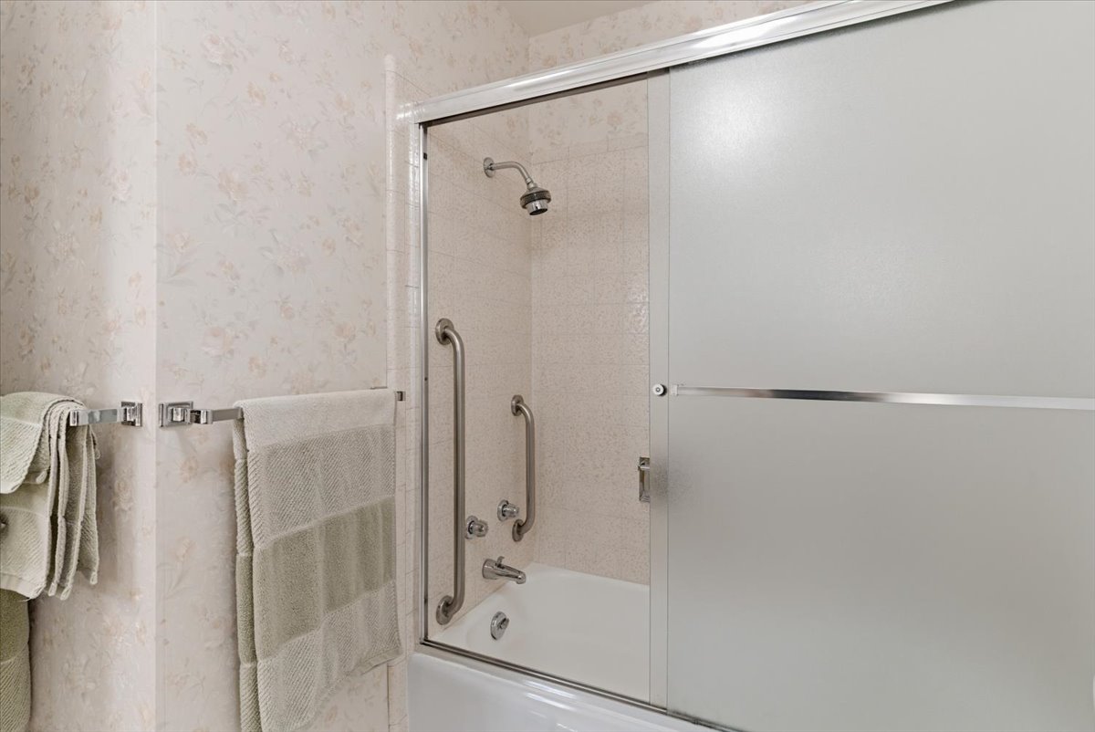 Bathroom featuring combined bath / shower with glass door and wallpapered walls