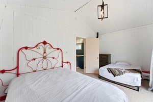 Carpeted bedroom with vaulted ceiling and wood walls
