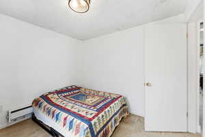 Bedroom featuring a baseboard radiator, light wood-style flooring, and a textured ceiling