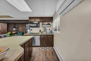 Kitchen with dark wood finish cabinetry, a baseboard heating unit, light countertops, a drop ceiling, and dark wood-style floors