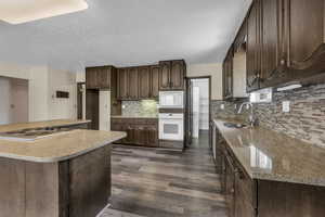 Kitchen featuring dark wood finish cabinets, white appliances, dark wood-style flooring, decorative backsplash, and light stone counters
