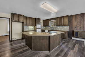 Kitchen featuring a center island, light stone counters, dark wood finish cabinets, dark wood-style flooring, and a textured ceiling