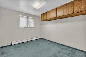 Carpeted spare room featuring a baseboard heating unit and a textured ceiling