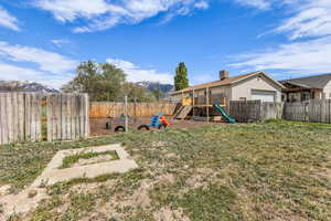 Fenced backyard featuring a playground, a mountain view, and a garage
