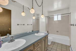 Bathroom with double vanity, light tile patterned floors, tub / shower combination, and a baseboard radiator