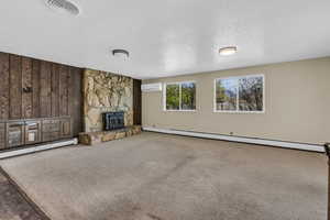 Unfurnished living room with baseboard heating, wood walls, carpet, and a textured ceiling