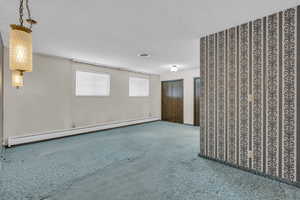 Unfurnished room featuring a baseboard heating unit, carpet flooring, and a textured ceiling