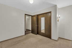 Unfurnished bedroom featuring light carpet, a closet, and a textured ceiling