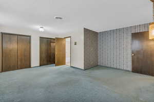 Unfurnished bedroom with multiple closets, carpet floors, and a textured ceiling