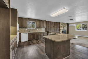 Kitchen featuring light countertops, dark wood-style floors, a center island, white appliances, and a textured ceiling
