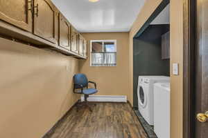 Laundry room with dark wood-style floors, baseboard heating, cabinet space, and washer and dryer