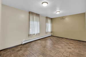 Empty room featuring a baseboard heating unit, parquet flooring, and a textured ceiling