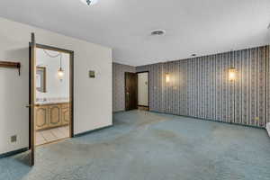 Empty room featuring light colored carpet, a textured ceiling, and wallpapered walls